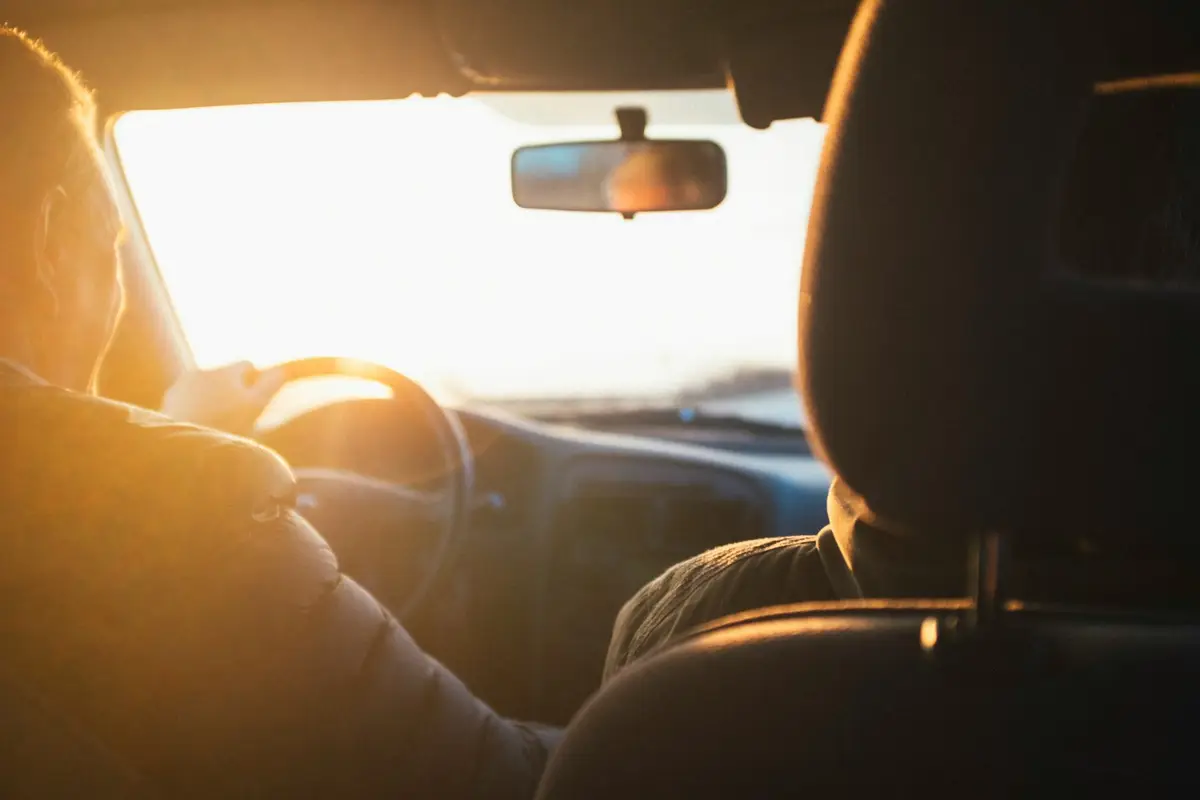 Motorista ao volante de um carro, com a luz dourada do fim de tarde entrando pelo para-brisa