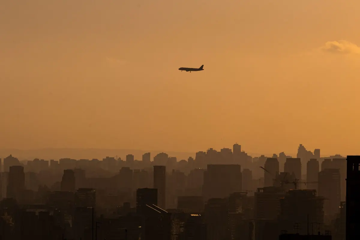 Avião se aproximando de São Paulo ao pôr do sol, sobre a silhueta dos prédios