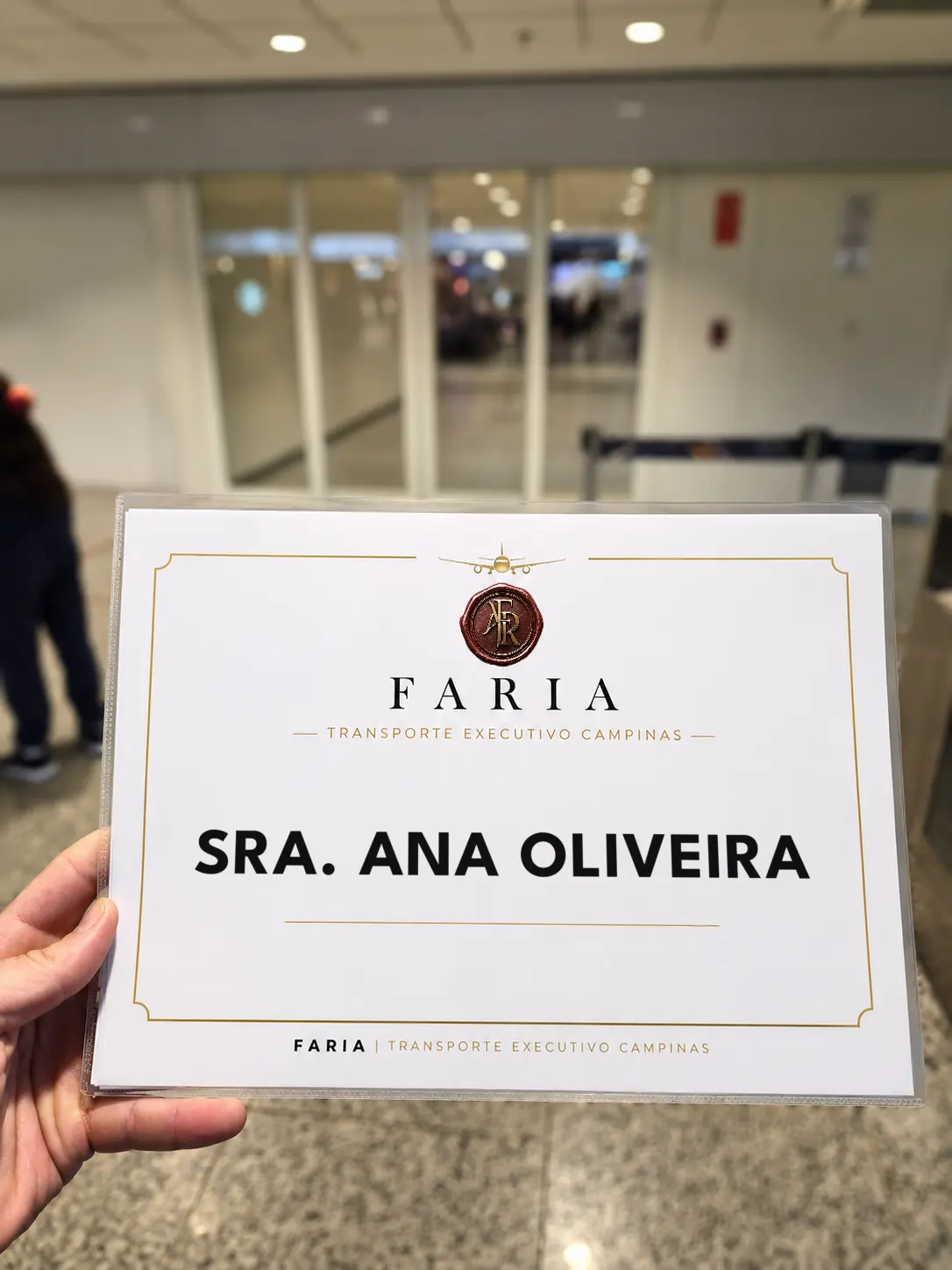 Placa de recepção da Faria Transporte Executivo erguida no saguão de desembarque de um aeroporto