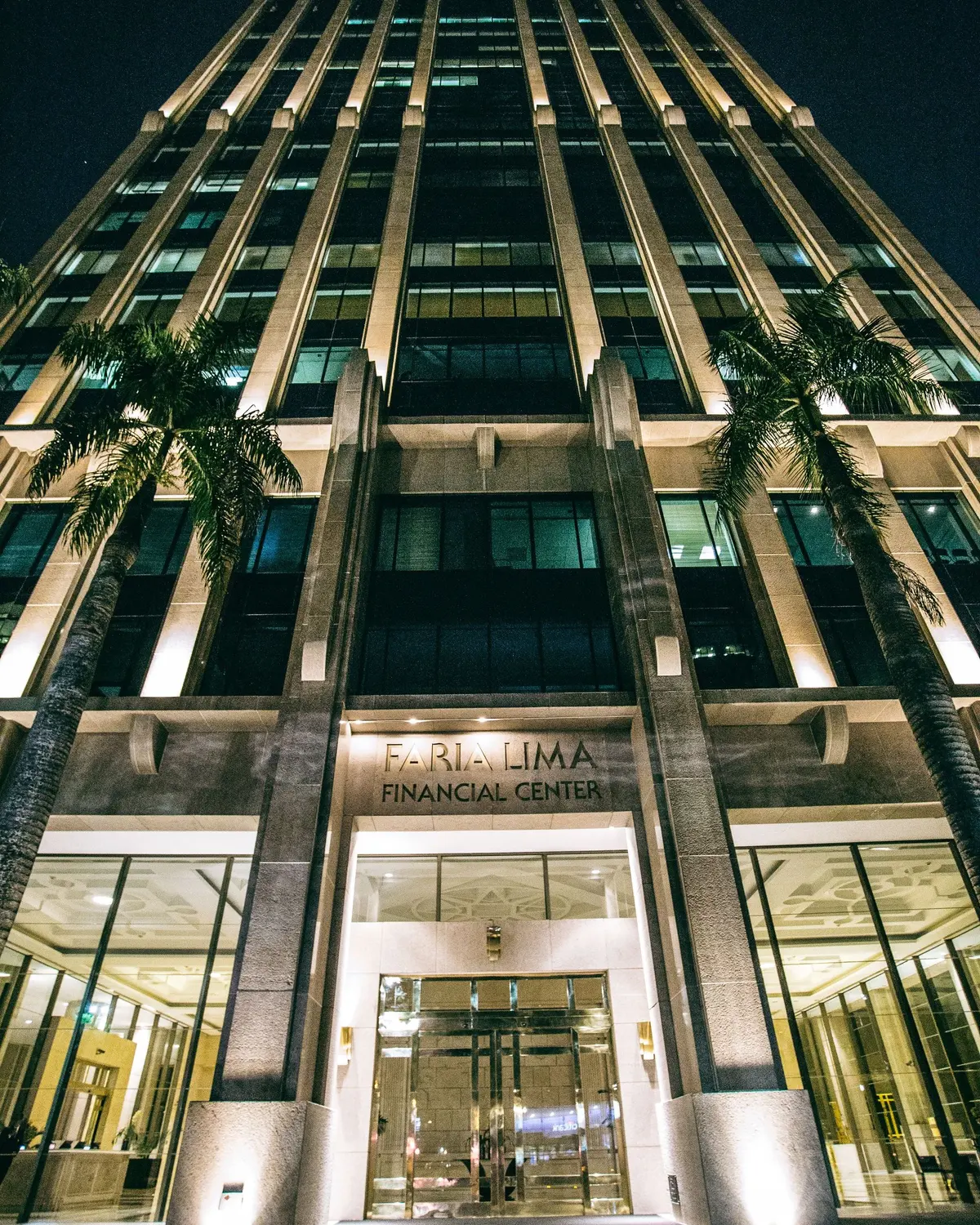 Fachada do Faria Lima Financial Center iluminada à noite, em São Paulo, com palmeiras na entrada