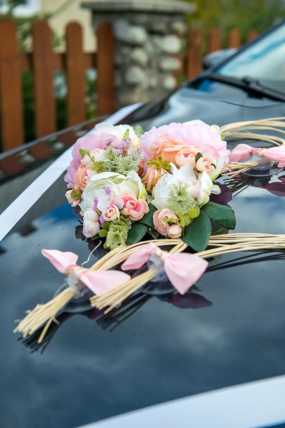 Arranjo de flores claras e laços cor-de-rosa sobre o capô de um carro de casamento