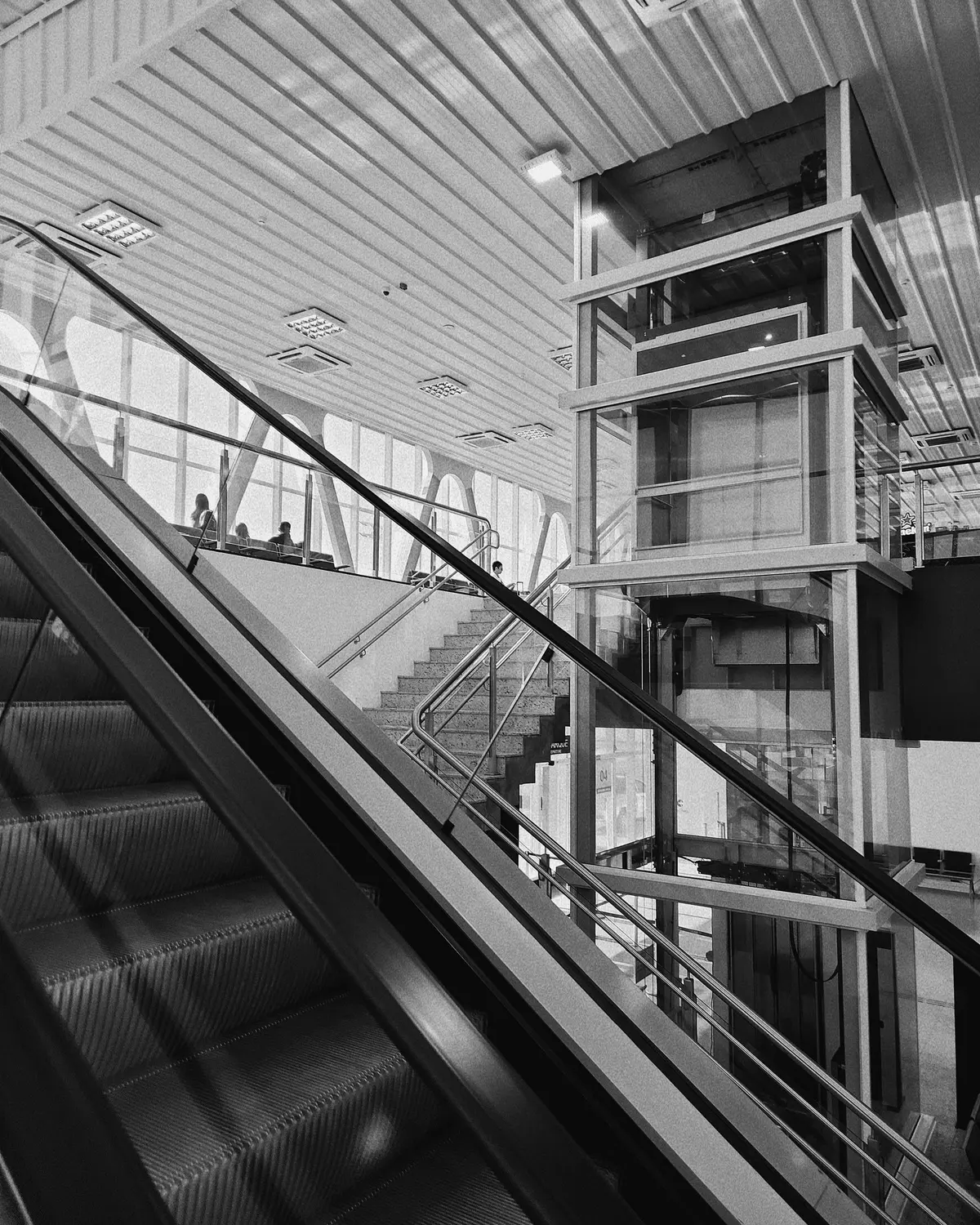 Saguão do Aeroporto Internacional de Guarulhos, com escadas rolantes e elevador panorâmico, em preto e branco