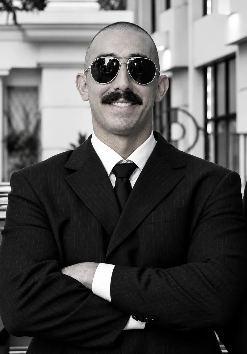 Motorista executivo de terno risca de giz, gravata e óculos de sol, de braços cruzados, em retrato em preto e branco